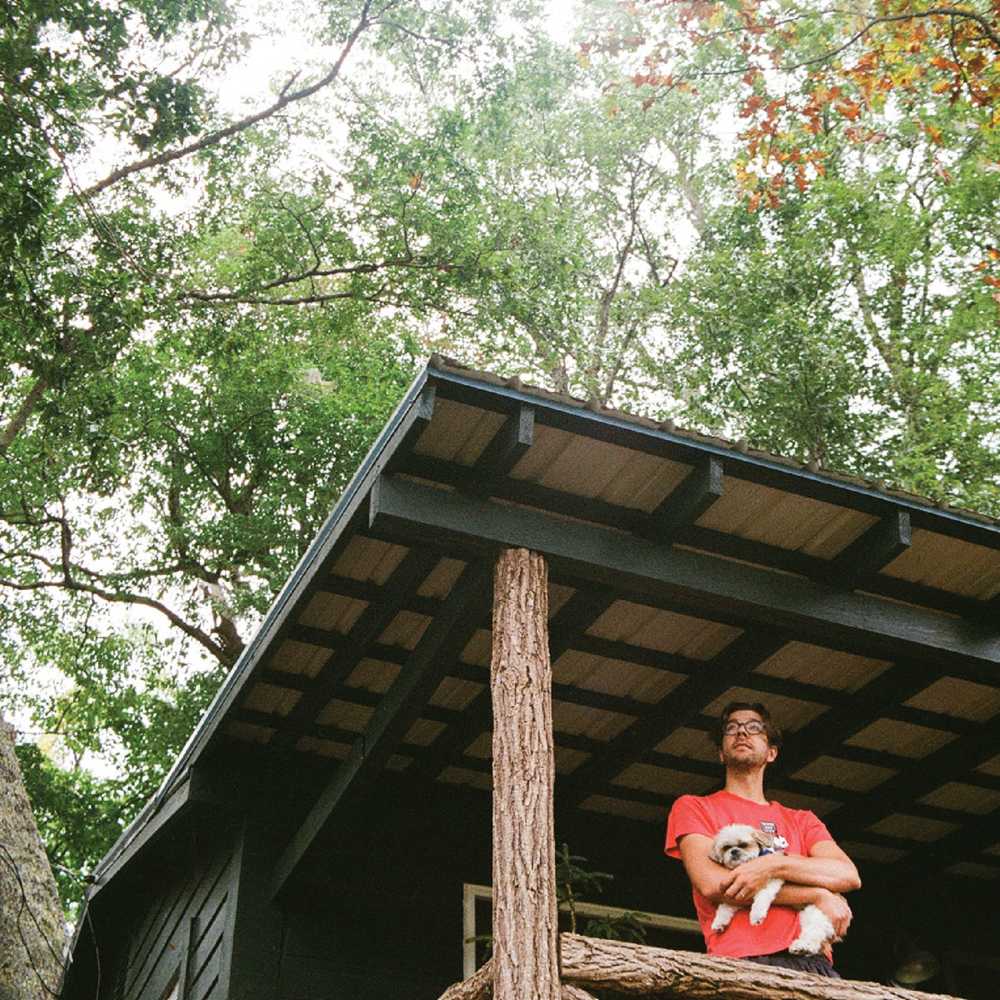 Matt holding his small fluffy dog on the porch of a cabin with a beautiful tree in the background.